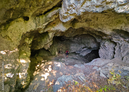 Fotografie Hiker exploring the large rocky entrance chamber of Három-kúti Cave in the Bükk Mountains, Hungary, surrounded by impressive limestone formations