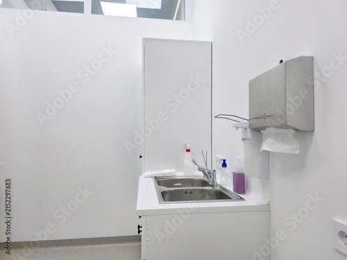 Stainless steel sink in a medical cabinet for hand washing. Professional hygienic facility with soap dispenser and paper towel holder. Clean clinical environment for healthcare hygiene.