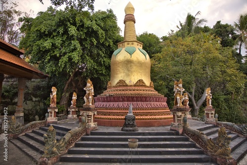 Obraz na plátně A magnificent golden stupa pagoda structure surrounded by stone guardian statues and dragon steps under a cloudy sky at the Brahma Vihara Arama buddhist monastery in Bali, Indonesia
