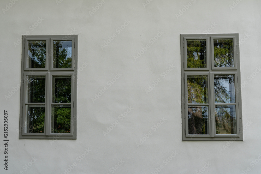 Fototapeta premium Two old, renewed grey wooden windows on white wall close up shot.