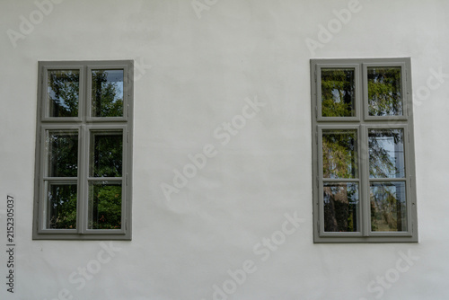 Two old, renewed grey wooden windows on white wall close up shot.