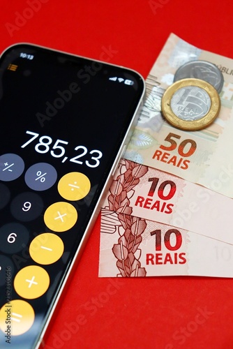 Smartphone displaying a calculator app next to Brazilian Real banknotes and coins. Brazilians financial planning and budgeting.