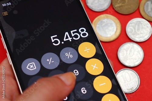 Person holding a smartphone with a calculator app open next to Brazilian Real money. Monthly budgeting, paying bills, and cost of living.