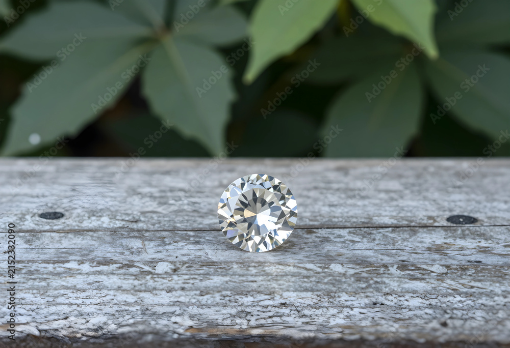 Obraz premium Brilliant cut diamond on weathered wooden surface with green leaves in soft focus background, the faceted gemstone reflects light, its clarity and sparkle