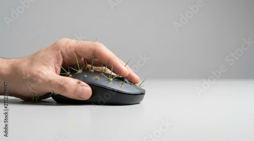 A hand is gripping a computer mouse that is covered in sharp green grass resembling cactus spines