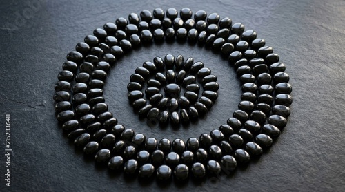 Smooth black obsidian pebbles arranged in a circular spiral pattern on a dark textured surface
