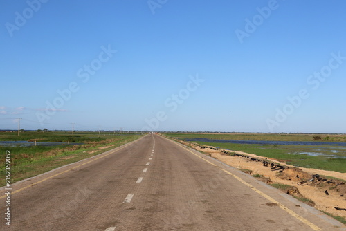 Scenic rural wetland and agricultural landscapes featuring shallow floodwater, green grasslands, open fields, dirt roads, palm trees and expansive blue skies. The images capture peaceful countryside