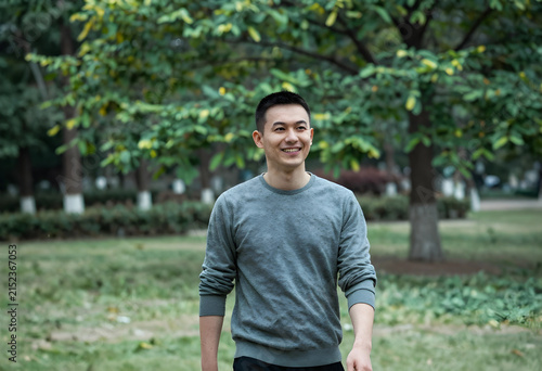 Smiling young asian man walking outdoors in a park, casual lifestyle and happiness concept, natural green background