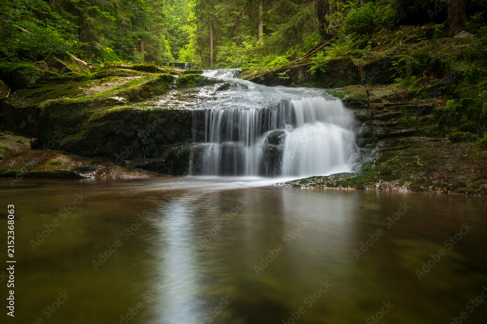 Fototapeta premium Small waterfall on the river flowing through a lush forest in the Jizera Mountains, Czech Republic, captured with a long exposure creating silky smooth water.
