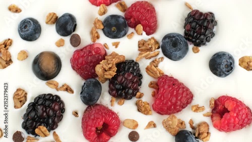 Granola falling down on greek yogurt with fresh berries, close up. Health protein breakfast concept