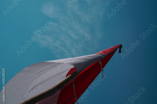 Indonesian national flag waving on a bamboo pole against a clear blue sky