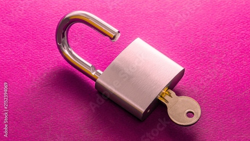Open silver padlock with brass key rests on vibrant pink background