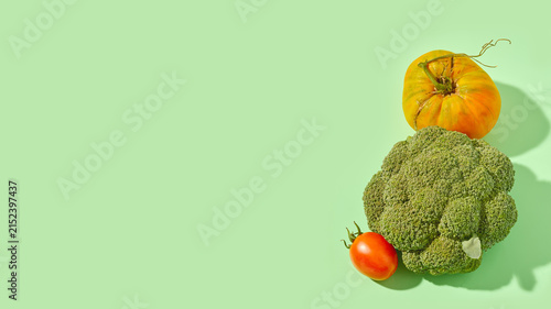 Fresh broccoli and yellow and red heirloom tomatoes arranged vertically on green studio background.