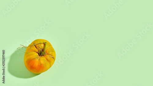 Yellow heirloom tomato on green background with copy space