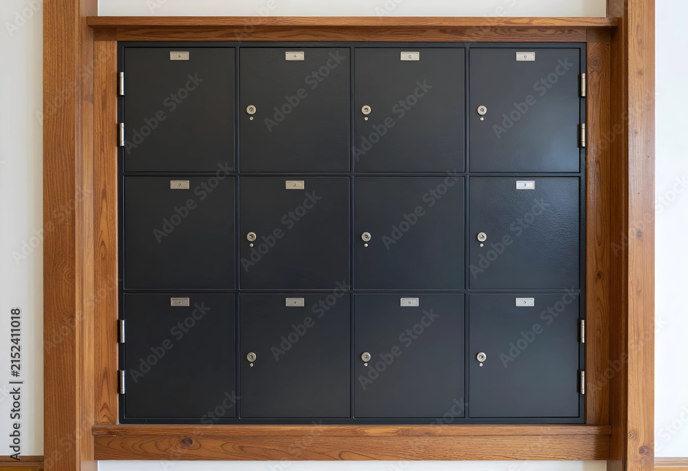 Fototapeta premium Wall of dark gray metal lockers with individual locks and number plates framed by natural wood trim, the locker unit is framed by natural wood trim, adding a warm architectural element