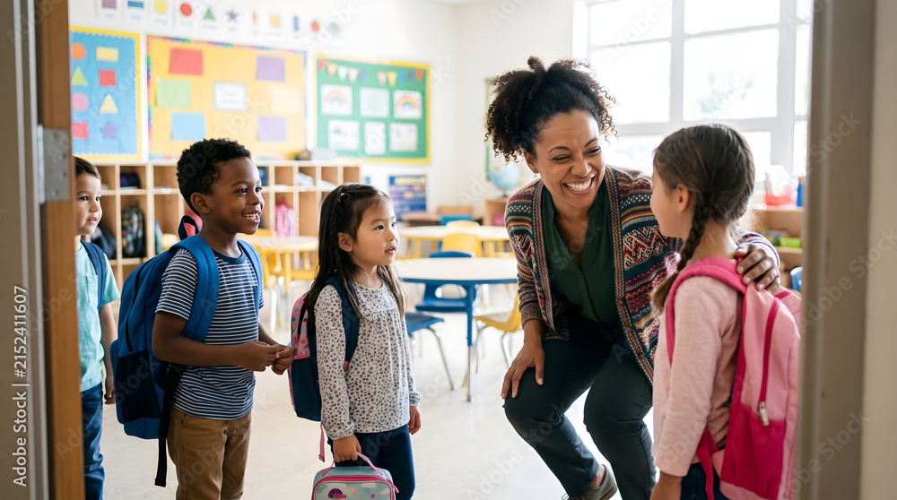 Fototapeta premium Smiling African American female teacher welcoming diverse young elementary school students wearing backpacks inside a bright modern classroom setting during their first day of primary learning