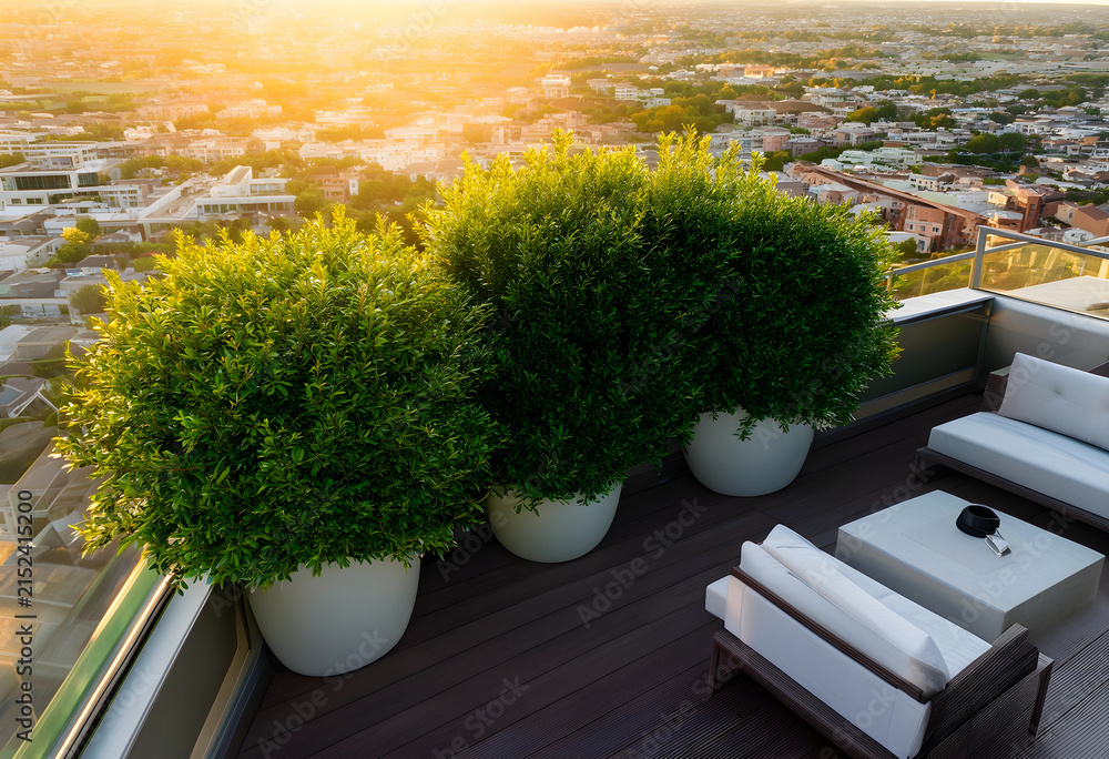 Obraz premium Rooftop terrace with potted green bushes and outdoor furniture overlooking a city at golden hour sunset, the modern urban landscape extends to the horizon under a warm, glowing sky