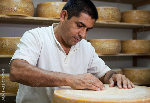 Artisan cheese maker inspecting a large wheel of aged cheese in a traditional aging cellar, food production and quality control