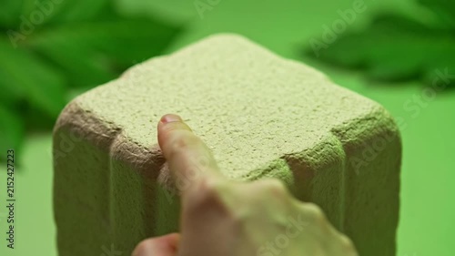 A person gently pressing their finger into a soft textured square foam block.