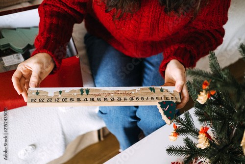 Quadro su tela Woman hand holds wooden MERRY CHRISTMAS countdown calendar with sliding tree marker near decorated tree