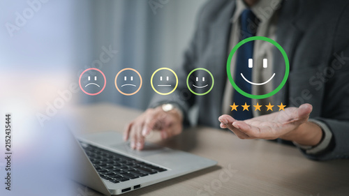 The hand is giving a five-star rating. The business person selects the smiley face icon on the virtual screen to express their satisfaction with the service. The rating received is very impressive.