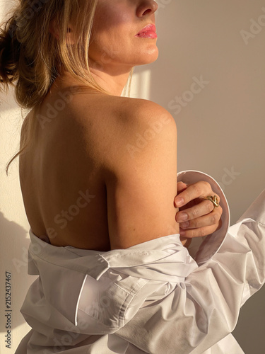 Serene woman in an oversized white shirt illuminated by warm natural light. Minimalist beauty and wellness concept expressing confidence, self care, healthy skin and timeless elegance.