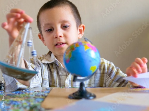 Curious schoolboy playing with toy boat and paper airplane while looking at globe illustrating imagination and geography travel