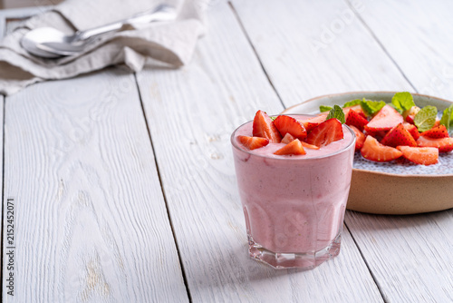 Glasses of strawberry smoothie on white wooden background