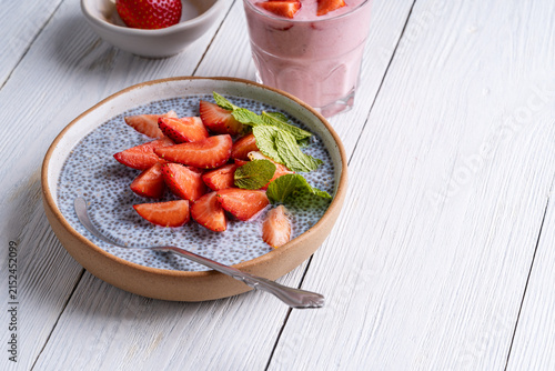 Chia seed pudding with kefir topped with sliced strawberry. Glass of strawberry smoothie on white wooden background