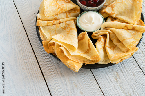 Folded crepes in black plate with berry preserves and sour cream on white wood background