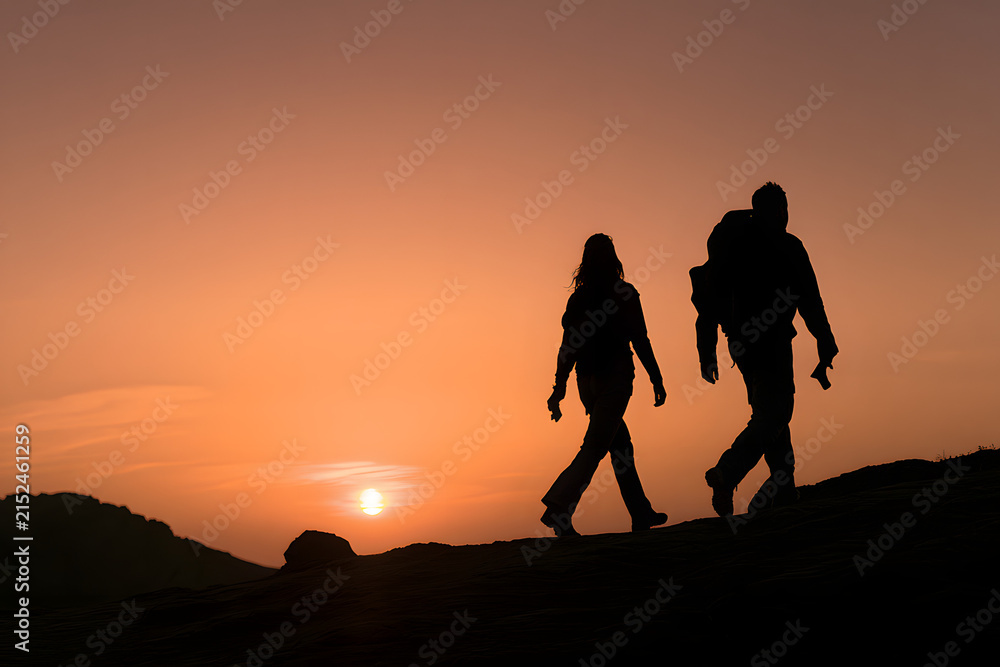 Obraz premium a couple in silhouette trekking through mountains as the sun sets