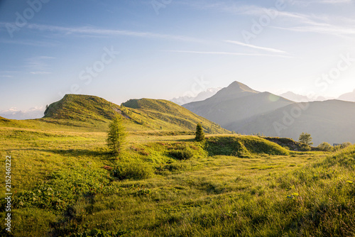 Bild auf Leinwand Expansive green mountain landscape with rolling hills and a distant mountain range under a clear sky