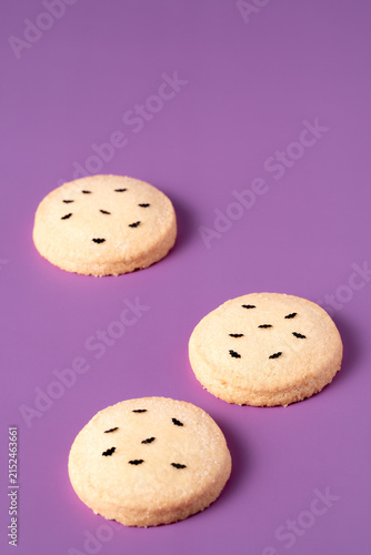Delicious Halloween cookies topped with edible black bat arranged diagonally on vibrant purple background with copy space for seasonal holiday marketing and party banner design