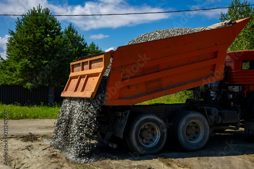 Canvastavla Orange dumper truck unloading crushed stone gravel on geotextile at construction site