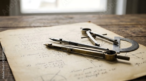 Vintage brass compasses and a protractor resting on aged parchment with handwritten mathematical calculations.