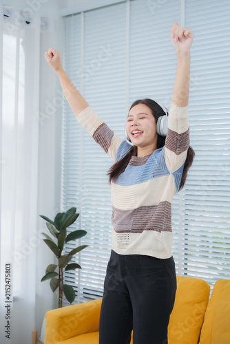 Konstfotografi Joyful Melody: A young woman with headphones on dances enthusiastically in her living room, hands raised in celebration to the beat of her favorite music, embodying pure, unadulterated happiness