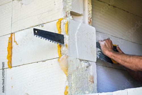 Construction builder worker cutting piece of foam insultation and brick at frame wall to make it straight, closeup detail