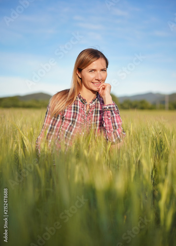 Young woman wearing a shirt crouching in unripe green wheat field, smiling