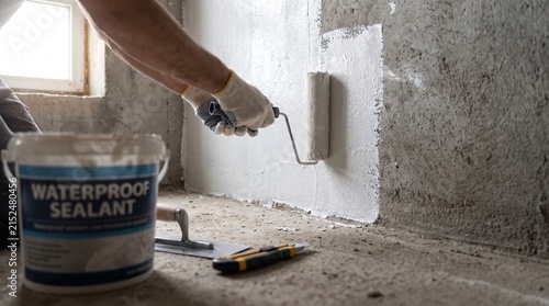 Worker applying waterproof sealant to a basement wall to reduce dampness.