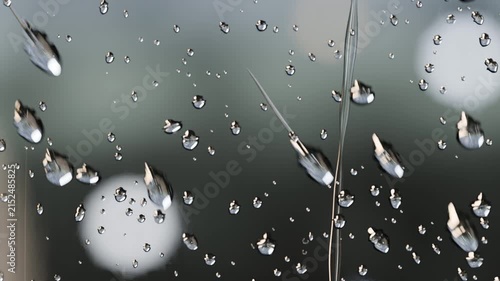 After merging droplets forming long streaks and sliding down glass, pulled by gravity with bokeh