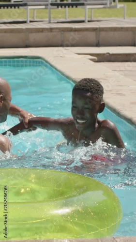 Vertical video: Youth reaching splashing climbing on adult in pool playing in red trunks green ring