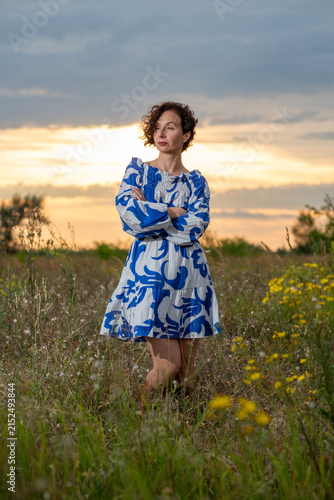 Woman in Blue Dress Standing in Wildflower Field at Sunset