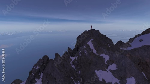 Person Standing Atop a Majestic Mountain Peak Under a Starry Night Sky