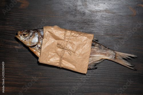 Dried salted fish wrapped in craft paper tied with twine. Top view of traditional stockfish roach wrapped in eco friendly brown paper on wooden background, beer snack food commercial concept