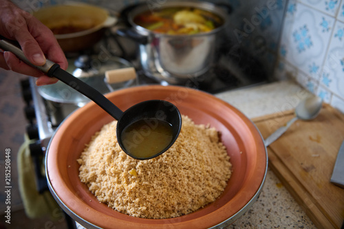 Authentic Moroccan couscous with vegetables being ladled with broth in a home kitchen