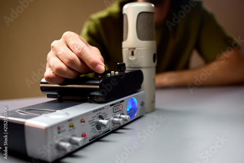 man adjusting settings on a professional audio interface in a focused studio environment with a green and black microphone and plastic and metal equipment close-up.