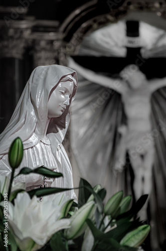 Фотография Virgin Mary Statue with White Lilies and Crucifix in Catholic Church