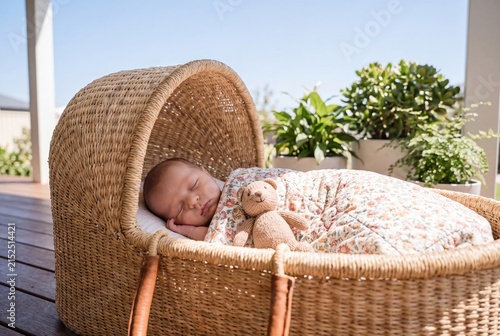 Sleeping newborn baby in wicker bassinet with teddy bear and blanket