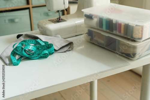 Картината върху платно A sewing machine on a white table with gray fabric and a measuring tape for preparation