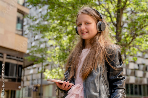 Принти на полотні Girl with long hair listens to music while standing outside in the city at dayti